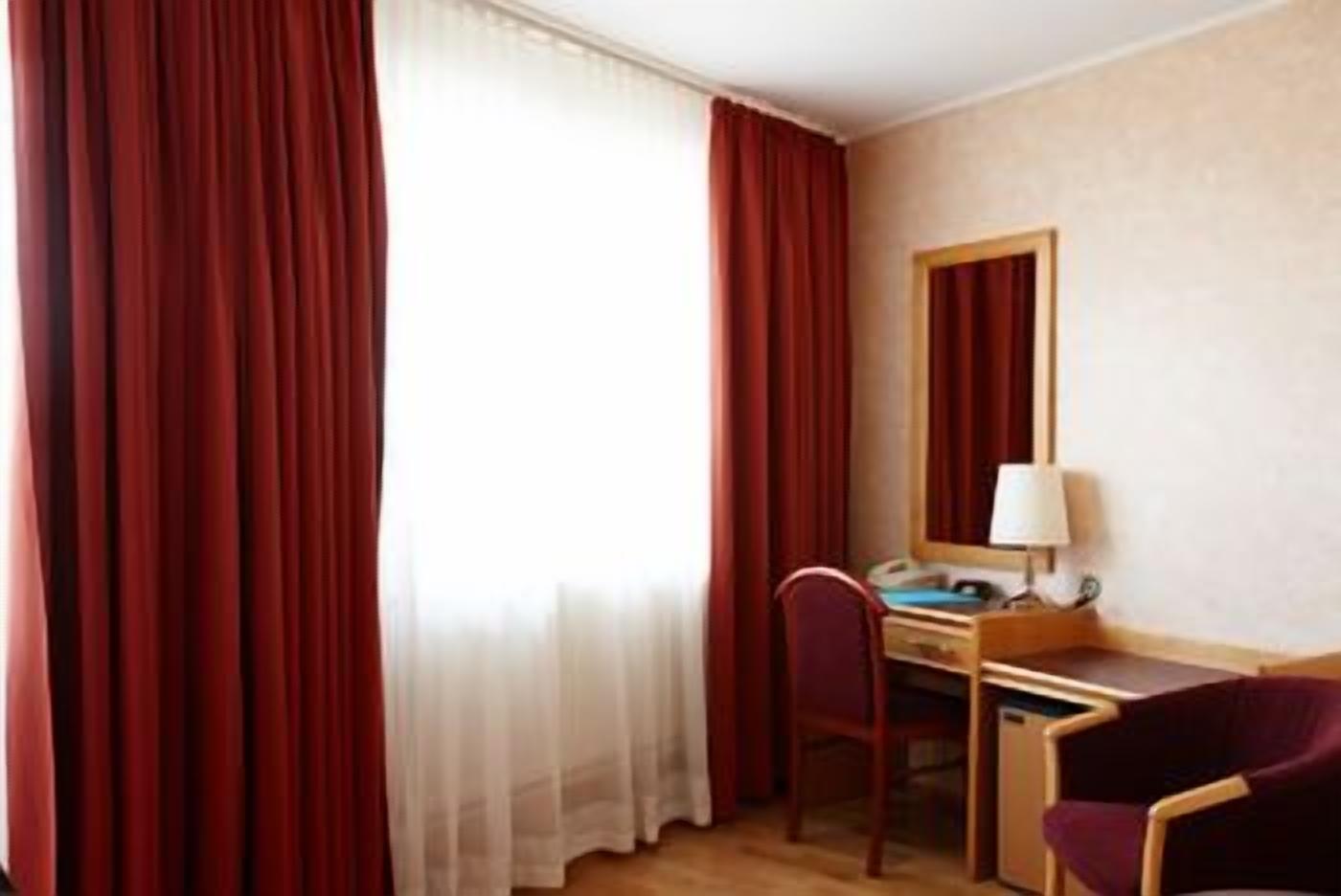 Una camera d'albergo con una scrivania, una sedia, una lampada e un grande specchio a parete.