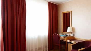 Una camera d'albergo con una scrivania, una sedia, una lampada e un grande specchio a parete.