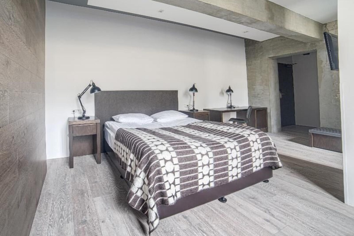 Egy modern hálószoba, melyben egy nagy ágy, két éjjeliszemélyzet lámpákkal, parketta és beton mennyezet található.
