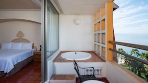 A balcony with a bed, a bathtub, and a view of the ocean.