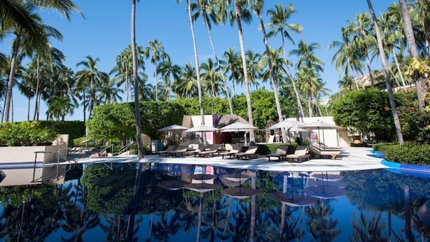 A resort pool area with palm trees, lounge chairs, and umbrellas.