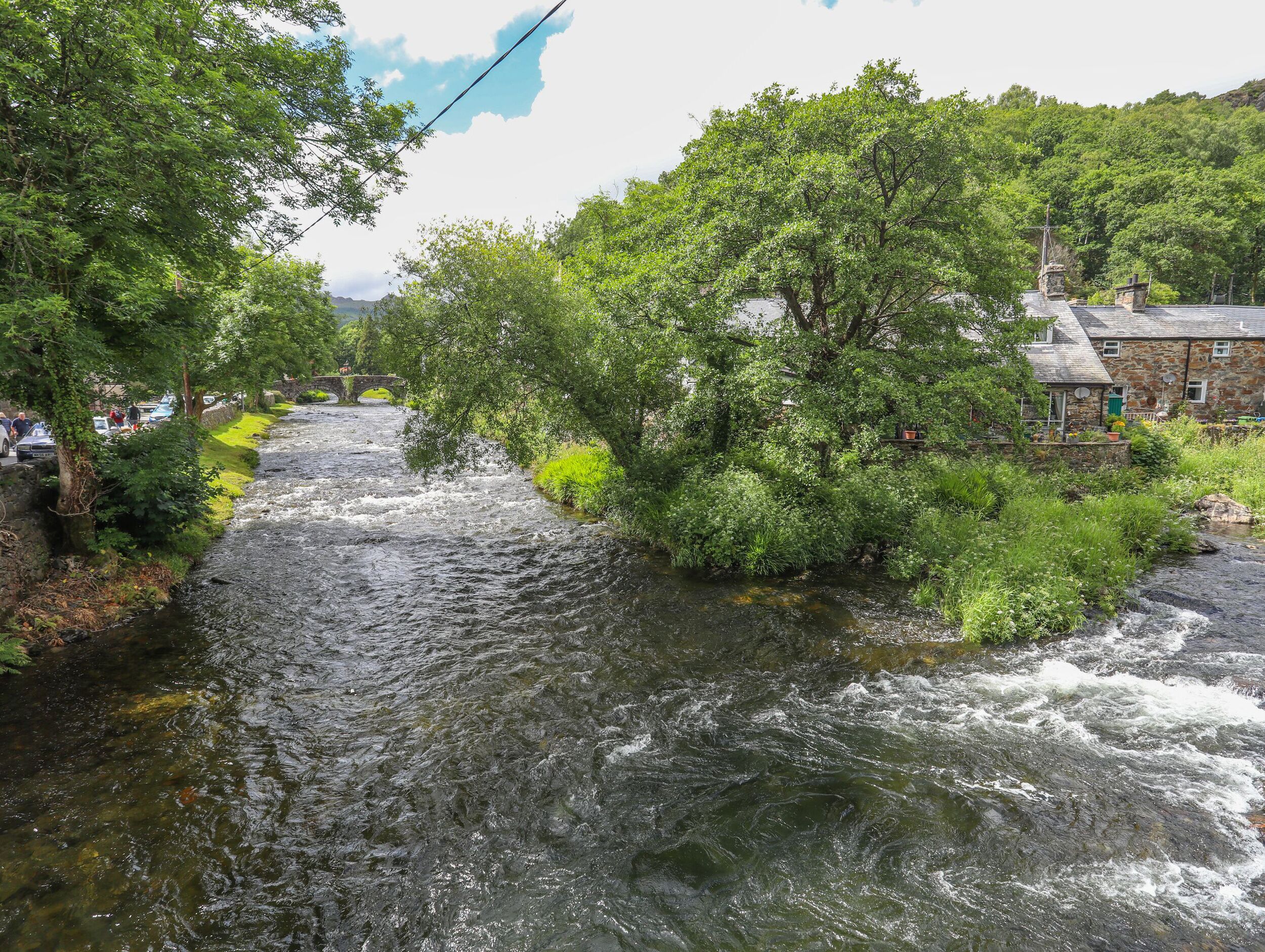 A river flowing through a lush, green landscape with stone buildings on one side.