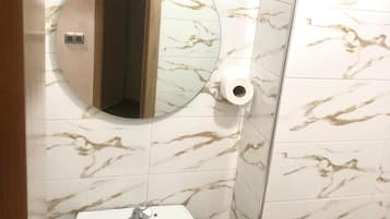 A bathroom with a marble-patterned wall, a round mirror, a sink with a faucet, and a toilet paper holder.