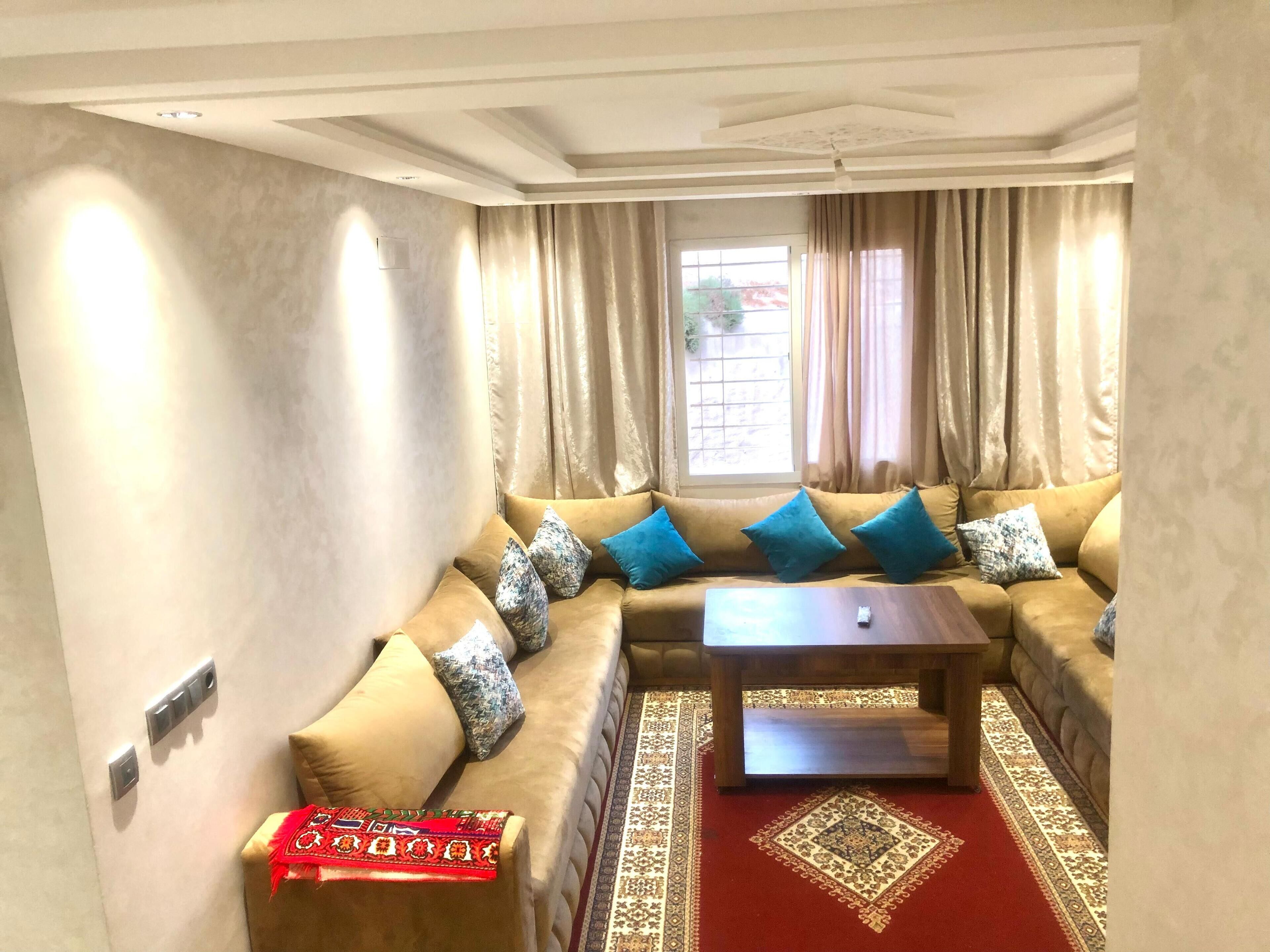 A living room with a beige sofa, blue cushions, a wooden coffee table, and a patterned rug.