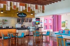 Un restaurante con mostrador, paneles de menú y zona de estar con mesas y sillas.