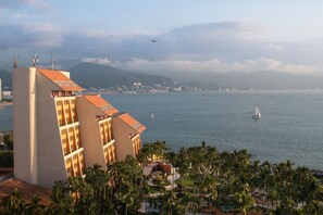 Un hôtel en bord de mer offrant une vue sur l’océan, un voilier et un avion au loin.