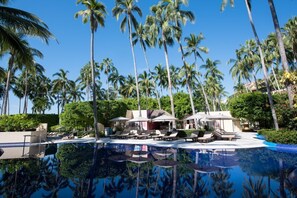 Poolbereich eines Resorts mit Palmen, Liegestühlen und Sonnenschirmen.