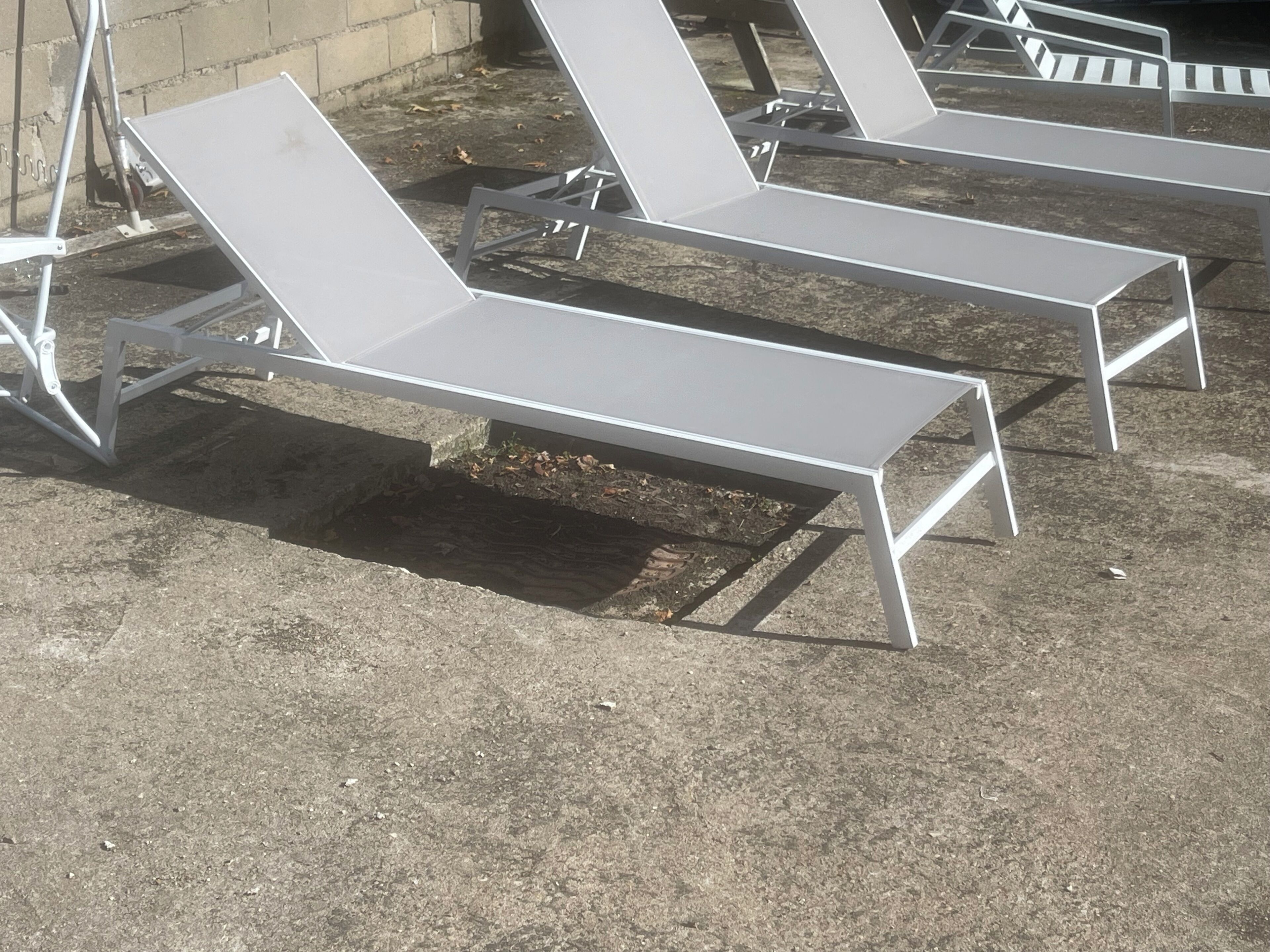 A row of white lounge chairs with metal frames, positioned outdoors on a concrete surface.