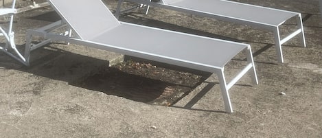 A row of white lounge chairs with metal frames, positioned outdoors on a concrete surface.