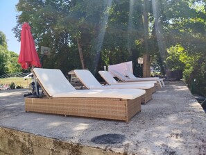Eine Reihe von Liegestühlen im Freien, mit Ziegelunterbau.