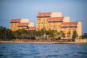 Um hotel com vários andares, localização à beira-mar e palmeiras.