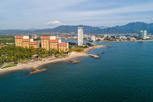 A coastal hotel with multiple buildings, a beach, and a mountainous backdrop. - Your Beachside Haven – 1BR Condo Near Everything (Puerto Vallarta)