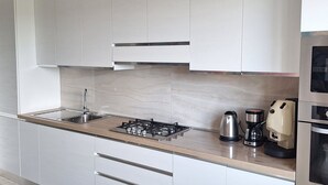 Une cuisine moderne avec des meubles blancs, un évier en acier inoxydable, une cuisinière à gaz, une machine à café et un four.