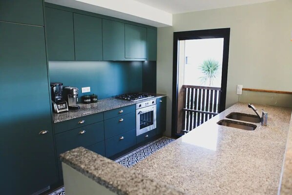 A kitchen with teal cabinets, a gas stove, a coffee maker, and a sink.