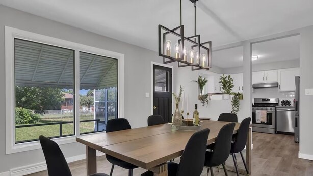 A modern kitchen with stainless steel appliances, a dining area with a wooden table and black chairs, and large windows offering a view of the outdoors. - Niagara Family Stay | Near Brock, Falls & Wineries (Thorold)