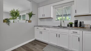 A modern kitchen with white cabinets, a granite countertop, and a window with blinds. - Niagara Family Stay | Near Brock, Falls & Wineries (Thorold)