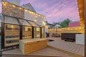 Une terrasse en bois avec un jacuzzi, un espace barbecue et des guirlandes lumineuses.