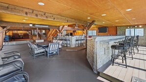 Een ruime binnenruimte met een houten plafond, een bar met krukken, en een zithoek met stoelen en tafels.