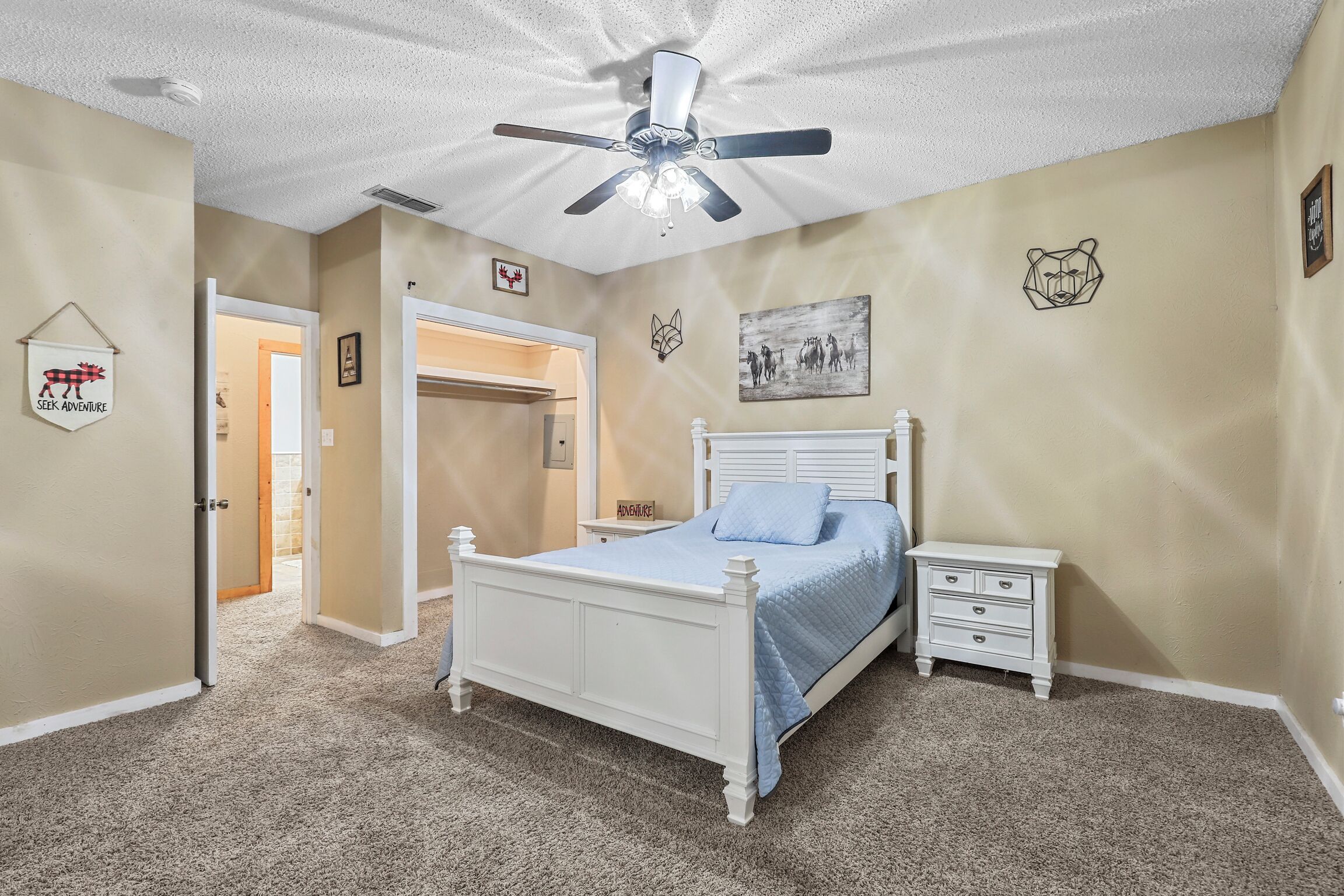 A bedroom with a white bed, a nightstand, a ceiling fan, and a door leading to another room.