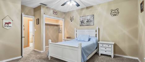 A bedroom with a white bed, a nightstand, a ceiling fan, and a door leading to another room.