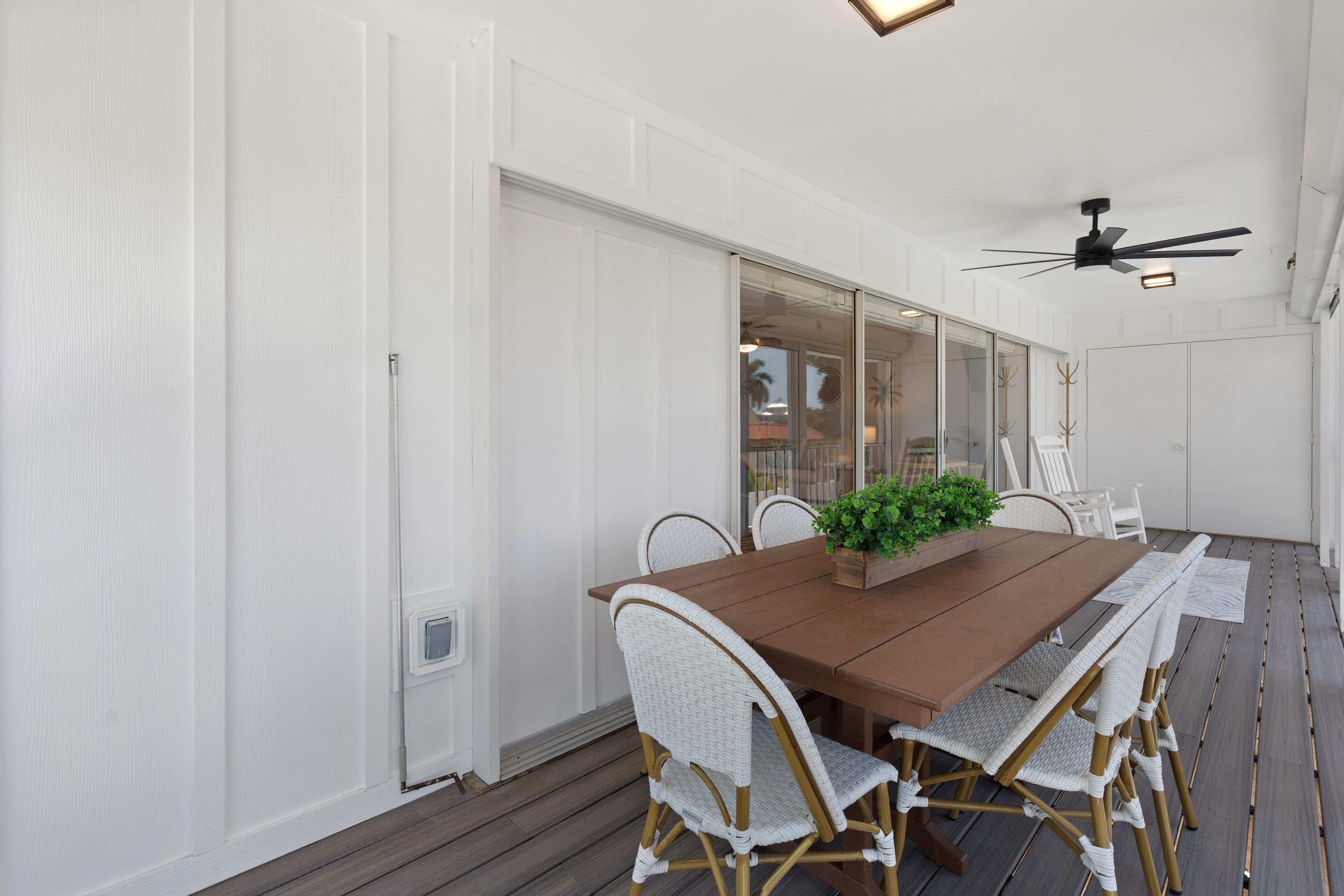 Spiseplads med et træbord, hvide fletstole og en loftsvifte.