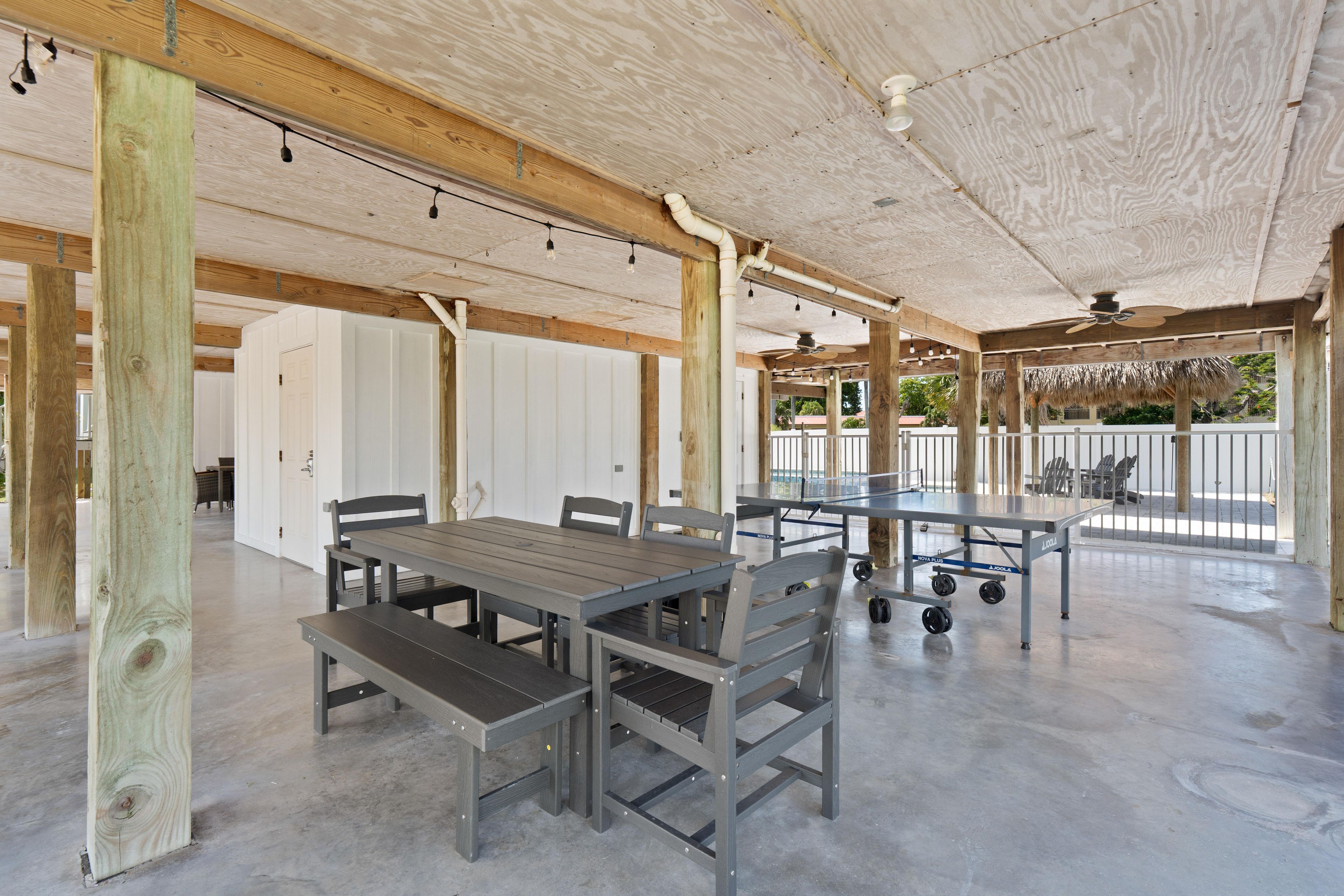 An outdoor covered patio area with tables and chairs, wooden beams, and a ceiling fan.