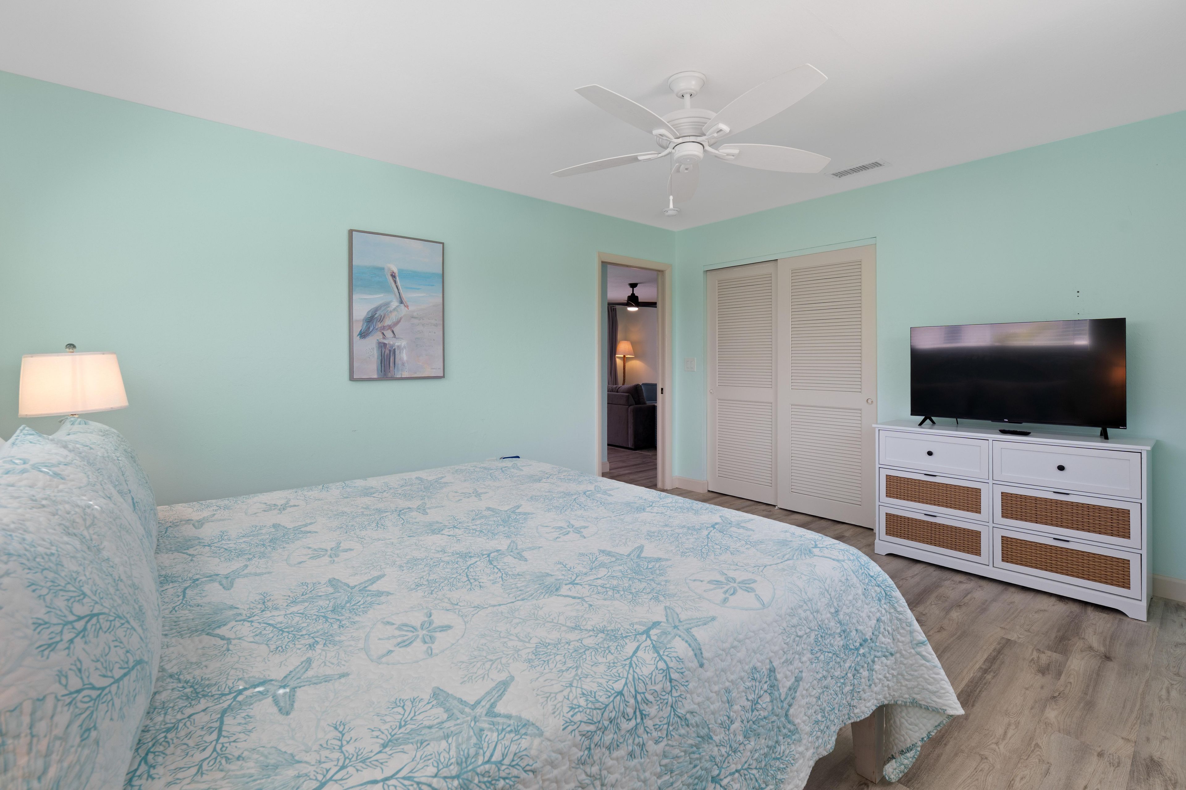 A bedroom with a bed, a ceiling fan, a television on a dresser, and a door leading to another room.