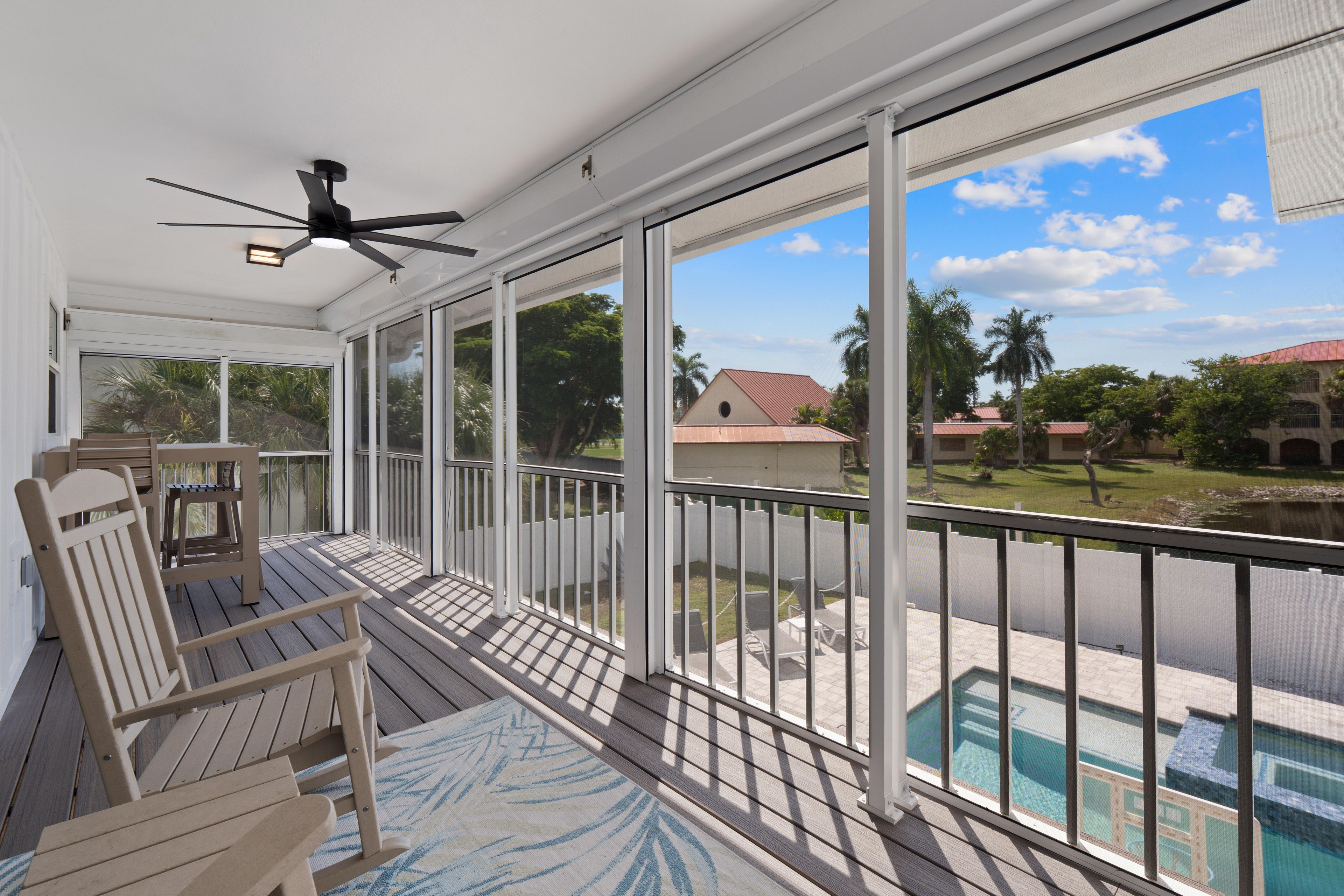 A covered outdoor area with a ceiling fan, a pool, and a view of a residential area with houses and palm trees.