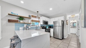 A modern kitchen with white cabinets, a stainless steel refrigerator, and a marble island. - Beachside Villas 1121 (Santa Rosa Beach)