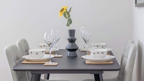 A dining table set with white plates, bowls, and wine glasses, centered by a vase with a single yellow flower. - Leven Loft -  2 Bed Flat in Coatbridge (Coatbridge)