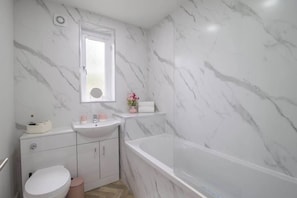 Un bagno con una parete in marmo, un lavandino bianco, un water e una vasca da bagno.