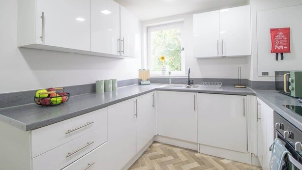 A modern kitchen with white cabinets, a herringbone floor, a sink, and a stove. - Leven Loft -  2 Bed Flat in Coatbridge (Coatbridge)
