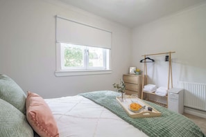 A bedroom with a bed, a window, a radiator, a drying rack, and a tray with a book and glasses.