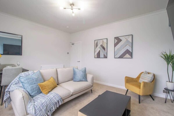 A modern living room with a sofa, armchair, coffee table, and artwork on the walls.