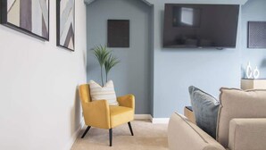 A living room with a yellow armchair, beige sofa, and a flat-screen TV mounted on the wall. - Leven Loft -  2 Bed Flat in Coatbridge (Coatbridge)