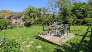 Une terrasse avec une table ronde et des chaises, entourée d’une pelouse et d’un jardin bien entretenus.