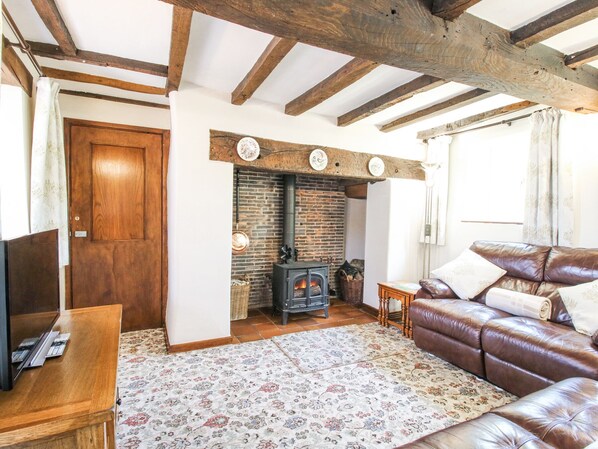 A cozy living room with a fireplace, wooden beams, a leather sofa, and a television.
