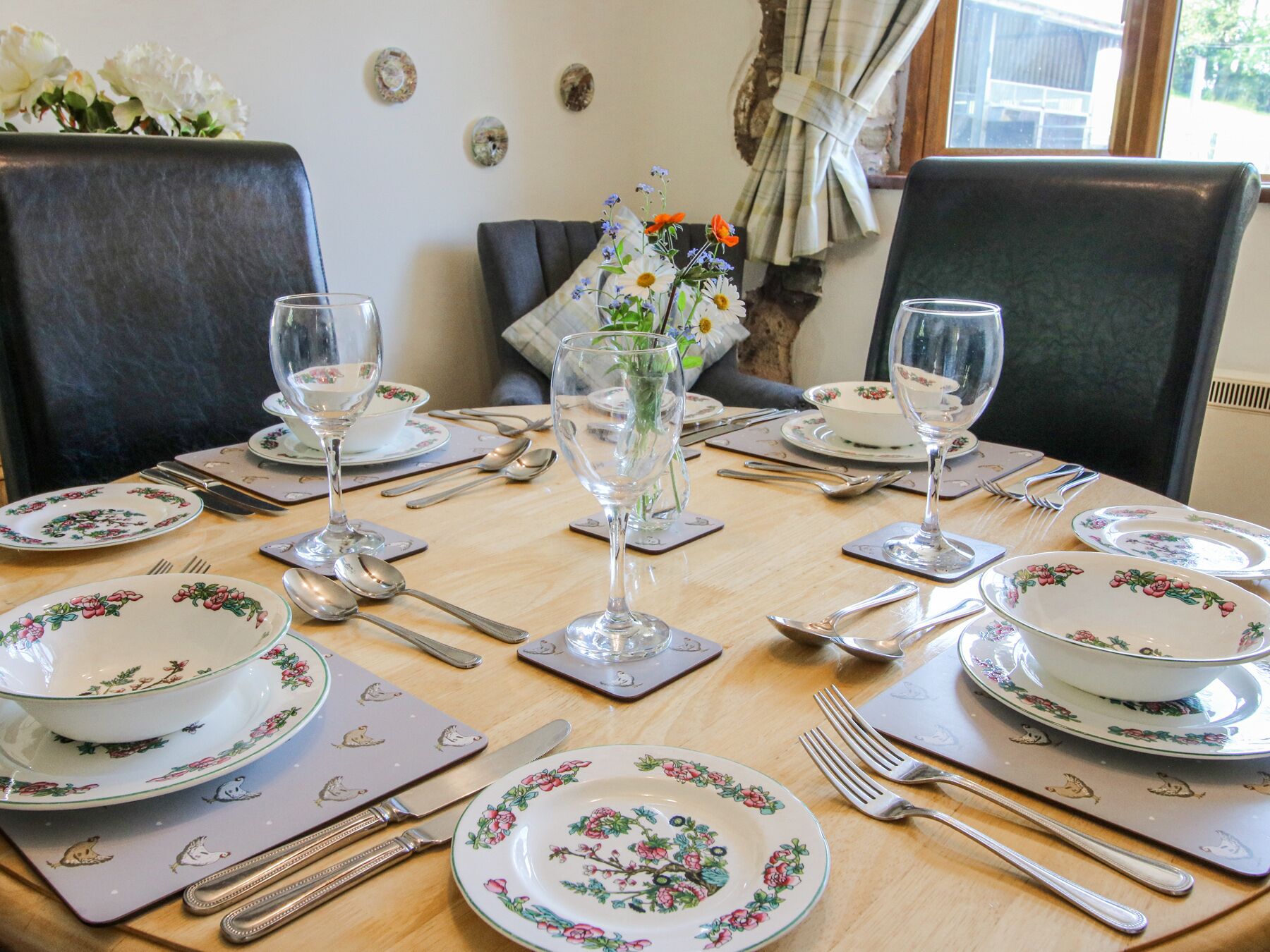 Ein Esstisch, gedeckt mit Geschirr mit Blumenmuster, Besteck und klaren Gläsern.