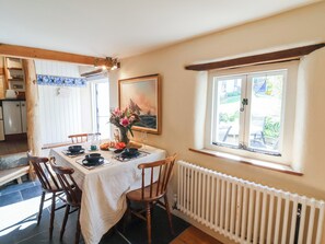 A dining area with a table set for four, a vase of flowers, a painting on the wall, and a window with a view of the outdoors. - Tadworthy Tower (Bideford)