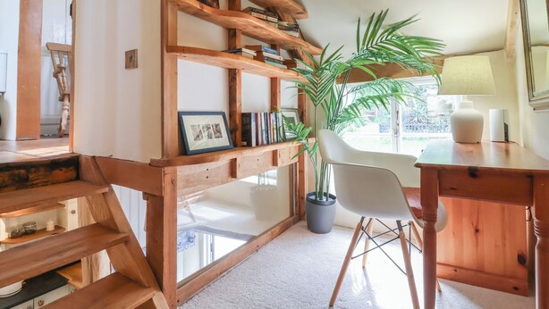 A cozy room with a wooden bookshelf, a potted plant, a white chair, and a desk with a lamp. - Tadworthy Tower (Bideford)