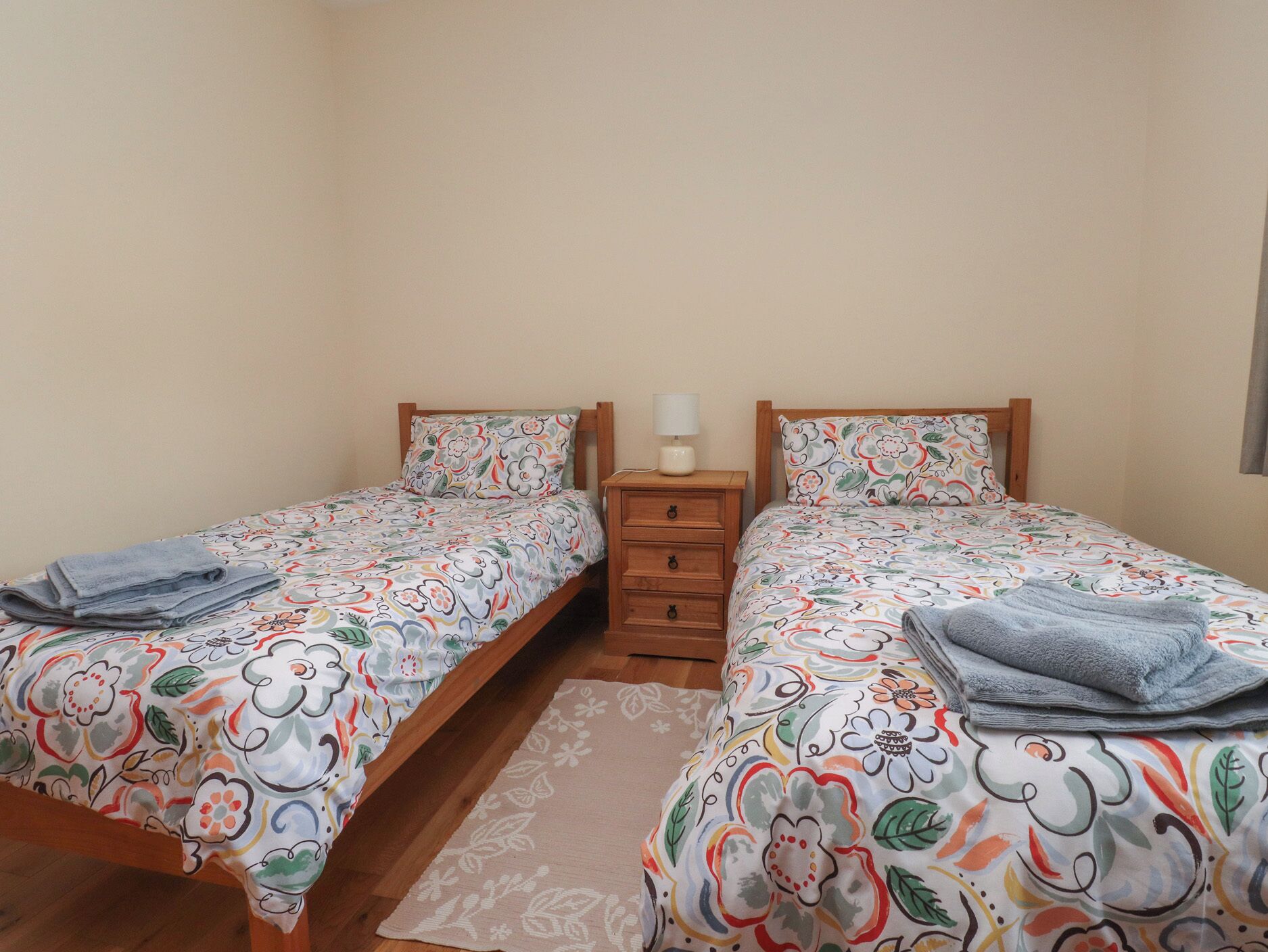 Une chambre avec un lit double, une literie à motifs floraux, une table de chevet en bois et une petite table de chevet avec une lampe.