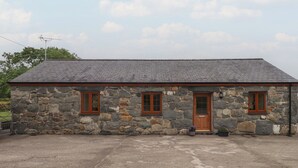 A stone building with a sloped roof, two wooden doors, and two windows. - Bryn Caled (Pwllheli)