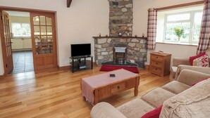 A cozy living room with a stone fireplace, wooden furniture, and a television on a stand. - Bryn Caled (Pwllheli)