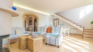 Un amplio salón con sofá, sillones a rayas, una mesa de centro y una escalera.