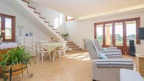 Un salón amplio con una escalera, una mesa de comedor con sillas, un sofá y un televisor.