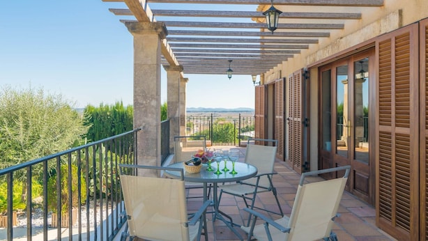 Un balcón con pérgola, mesa y sillas al aire libre, y vista del paisaje.