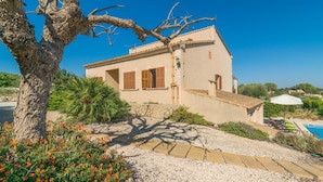 Una casa de dos pisos con un camino de piedra que conduce a la entrada, rodeada de vegetación y una zona de piscina.