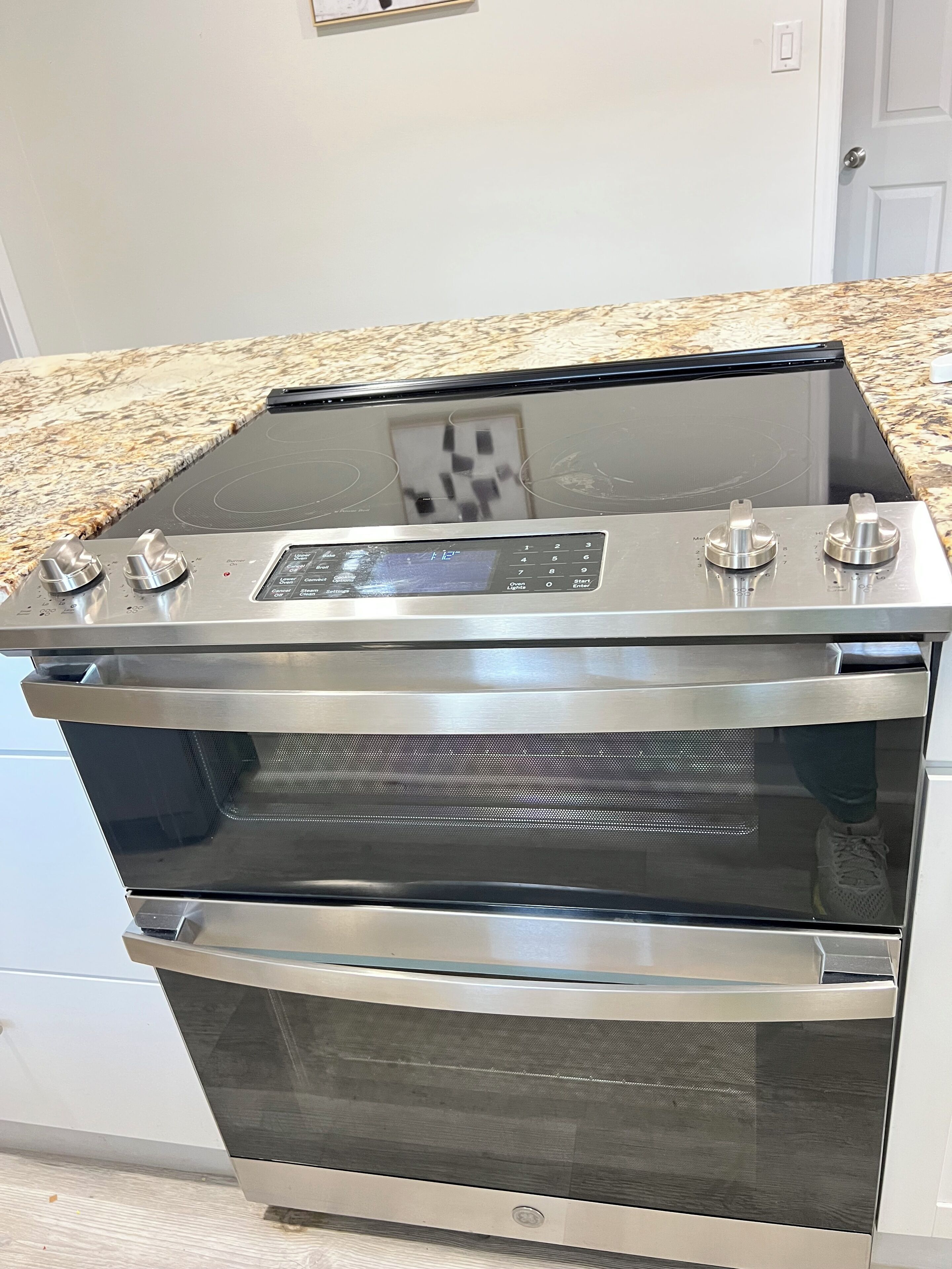 A stainless steel oven with a digital control panel and two knobs, located in a kitchen with a granite countertop.
