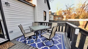 A deck with a glass-top table and four chairs, surrounded by a wooden deck and a blue patterned rug. - HP@The Cottage|Spectrum|Bojangles|NODA|Dogs|Yard (Charlotte)