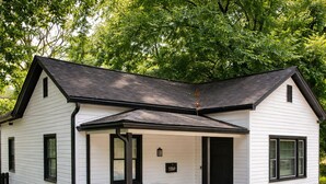 A single-story house with a porch, a black front door, and a small window. - HP@The Cottage|Spectrum|Bojangles|NODA|Dogs|Yard (Charlotte)